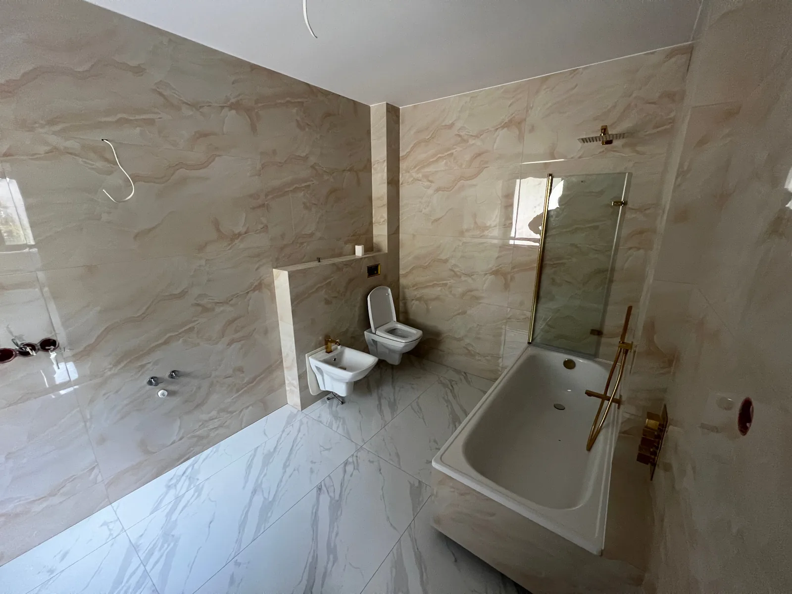 Łazienka w trakcie wykończenia: jasna glazura, wanna ze złotą armaturą, toaleta i bidet